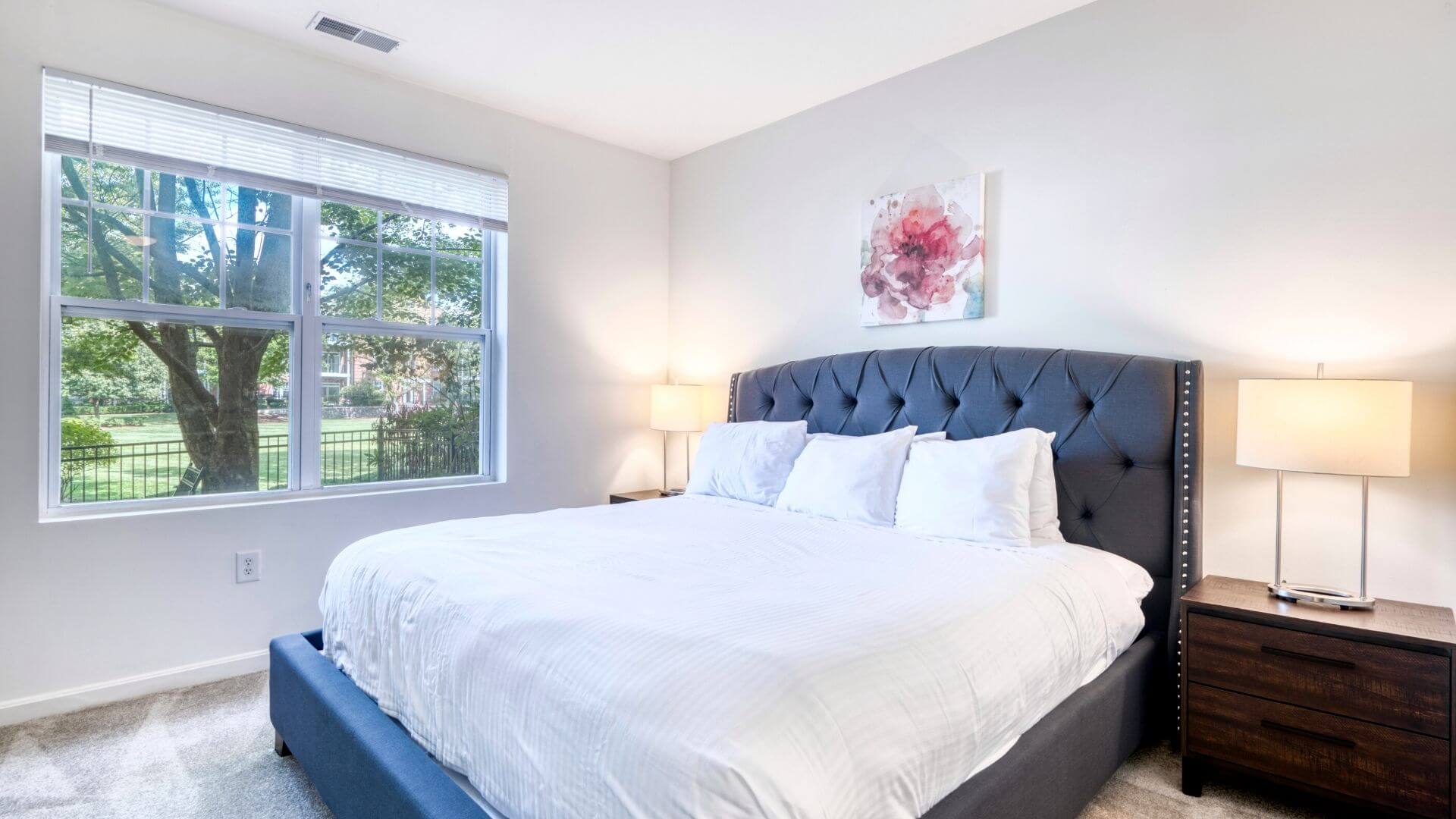 Large freshly made bed with crisp linens and trees outside the window