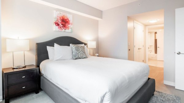 Freshly made comfortable bed in a room with a view through to the hall and artwork hanging on the wall.