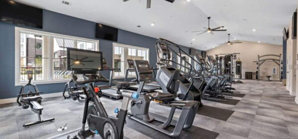 The Avery by Compass Furnished Apartments — Modern fitness center featuring cardio machines, spin bikes, treadmills, and stair climbers in a bright, well-equipped gym space