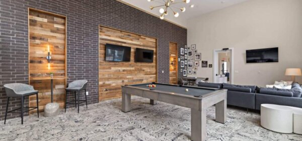 Stylish game and lounge room at The Avery by Compass Furnished Apartments, featuring a modern pool table, flat-screen TVs, and cozy seating areas with wood and brick accents.