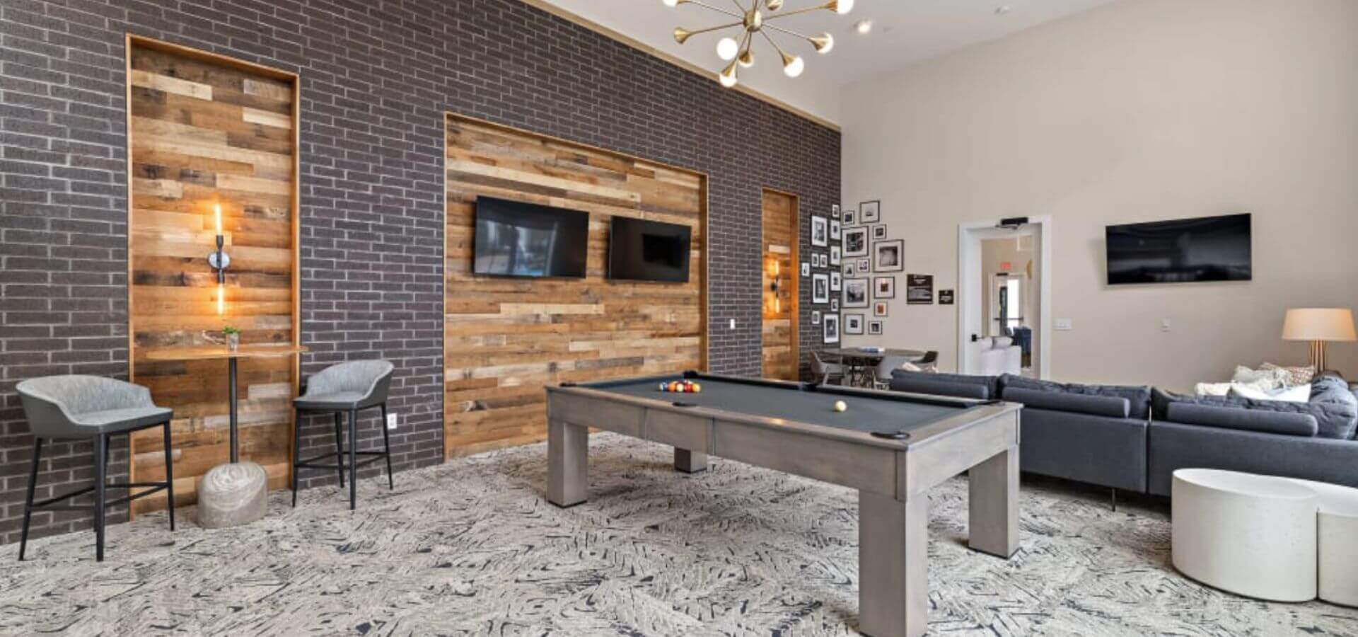 Stylish game and lounge room at The Avery by Compass Furnished Apartments, featuring a modern pool table, flat-screen TVs, and cozy seating areas with wood and brick accents.