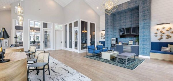 Bright and modern lounge area at The Avery by Compass Furnished Apartments, featuring high ceilings, stylish blue accents, and a refreshment station with seating.