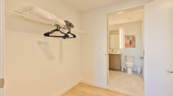 Spacious walk-in closet with shelving and hangers leading to a modern bathroom at Compass Furnished Apartments in Idyl Fenway—thoughtfully designed for long-term comfort.