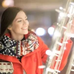 Woman in a red coat smiling while enjoying winter holiday lights in Stamford