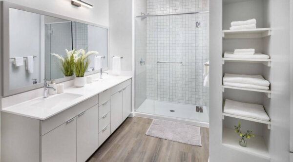 Spacious bathroom at The 305 with double vanity, glass walk-in shower, and built-in shelving – Compass Furnished Apartments.