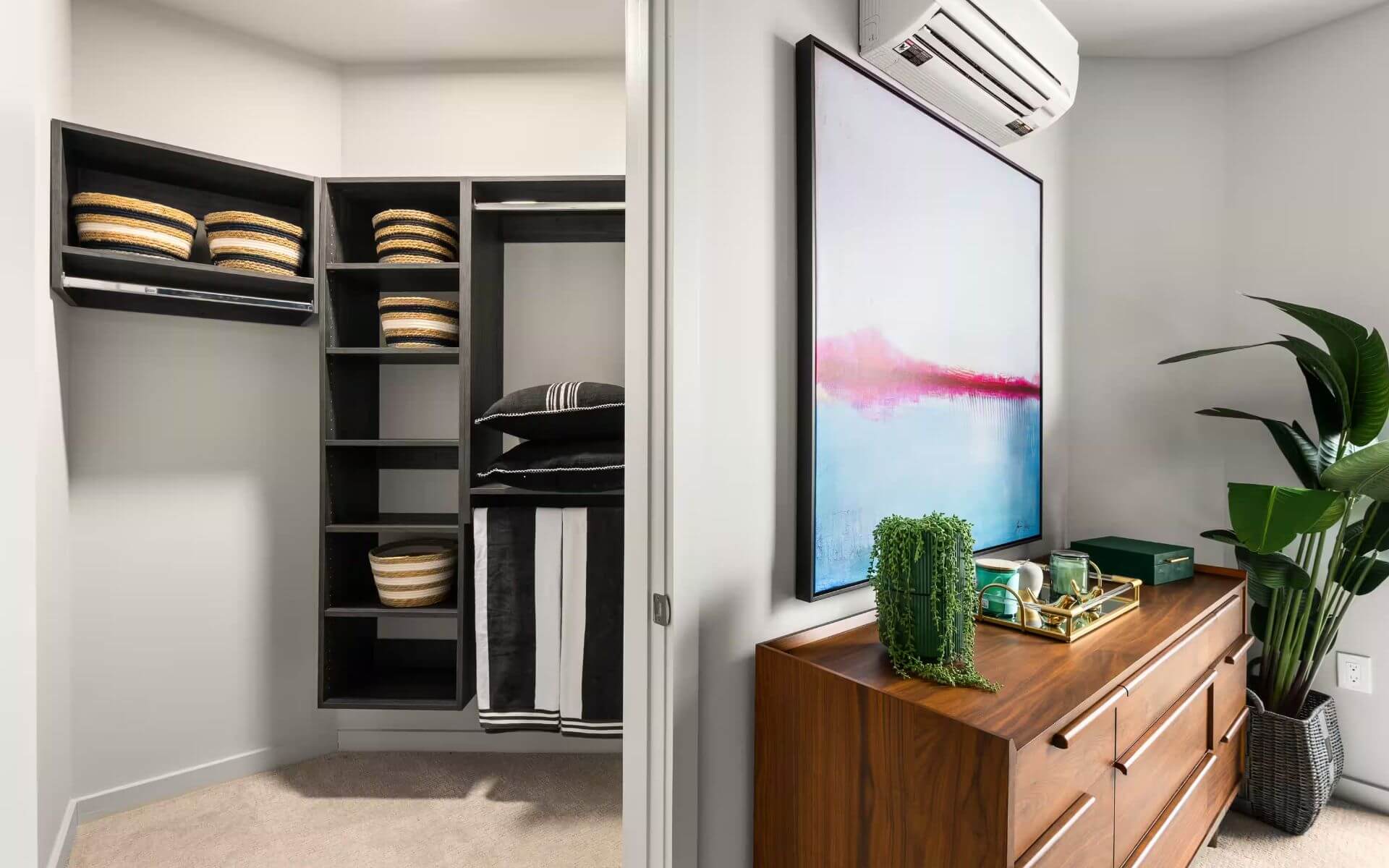 Spacious walk-in closet with open shelving, woven baskets, and a wooden dresser topped with decor accents at 51 South by Compass Furnished Apartments.