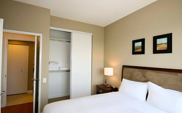 Cozy bedroom at MAC Garden by Compass Furnished Apartments, featuring a plush bed with crisp white linens, built-in closet with extra towels, soft lighting, and minimalist wall art.