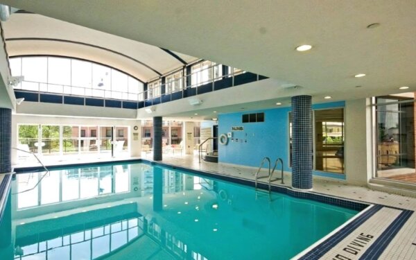 Spacious indoor pool at MAC Garden by Compass Furnished Apartments, featuring arched ceilings, tiled columns, and floor-to-ceiling windows that fill the area with natural light.
