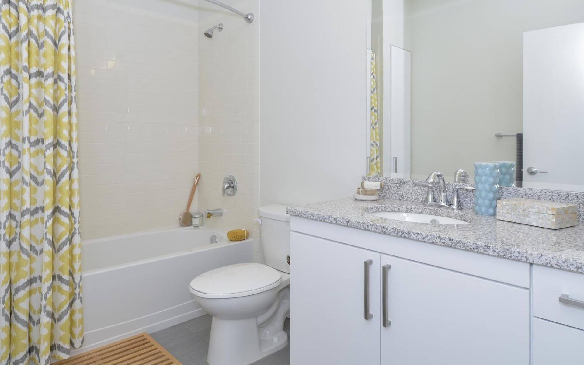 Bright bathroom at 75 Tresser by Compass Furnished Apartments featuring granite countertops, modern fixtures, and a patterned yellow shower curtain.