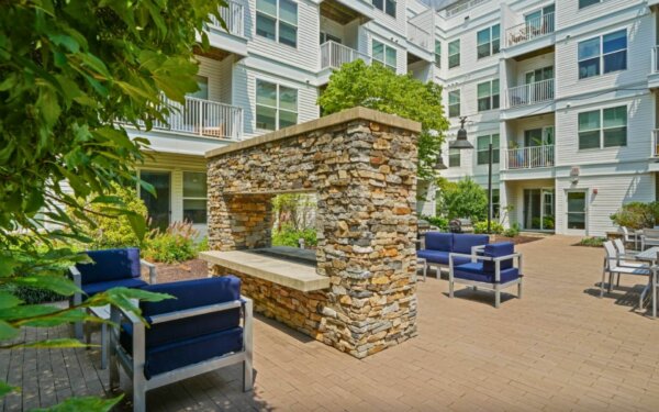 Outdoor lounge with stone fireplace and blue cushioned seating at 75 Tresser by Compass Furnished Apartments.