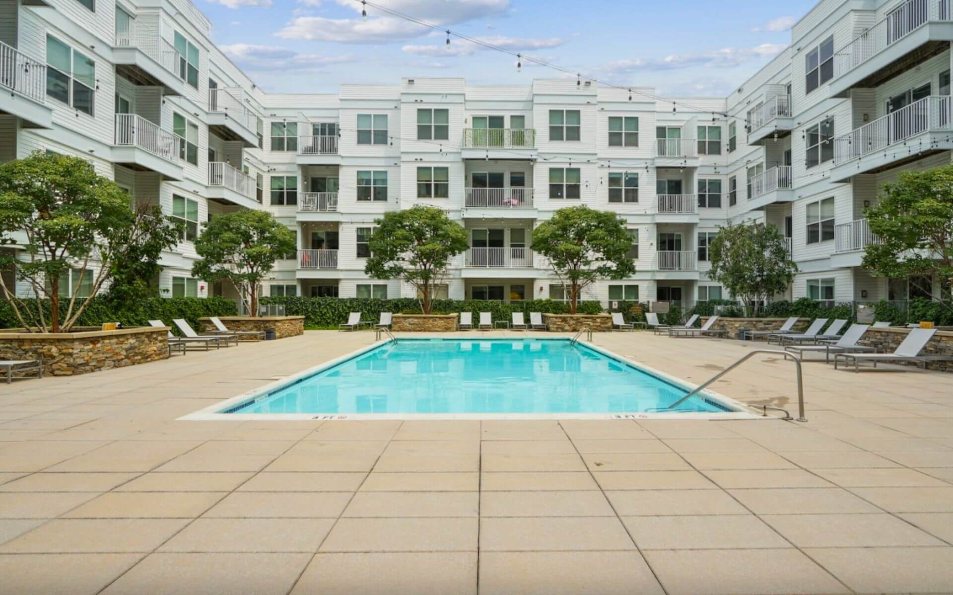 Sparkling outdoor swimming pool surrounded by lounge chairs at 75 Tresser by Compass Furnished Apartments.
