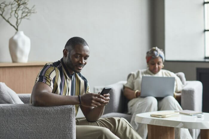 Man using a smartphone and woman working on a laptop in a modern furnished apartment living room.