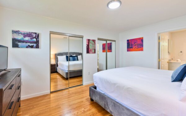 Spacious bedroom with mirrored closets, hardwood floors, and modern décor at Compass Furnished Apartments, 235 Cardinal Medeiros.