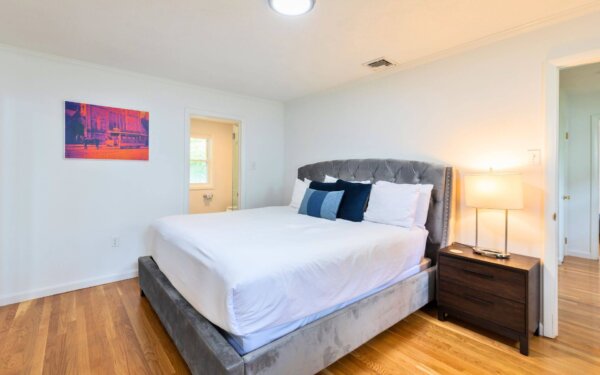 Cozy bedroom with modern upholstered bed, wood nightstand, and ensuite bathroom at Compass Furnished Apartments, 235 Cardinal Medeiros.