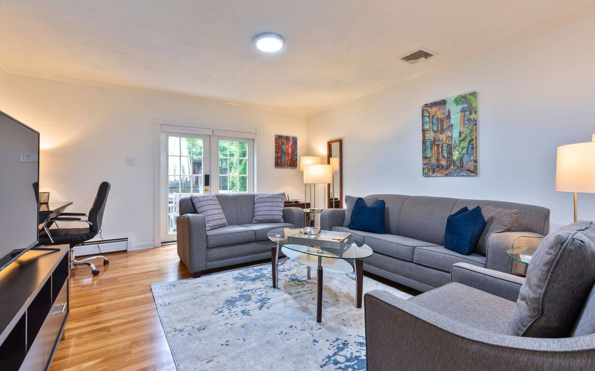 Stylish living room at 235 Cardinal Medeiros with modern grey furniture, work desk, French doors to patio, and contemporary artwork.