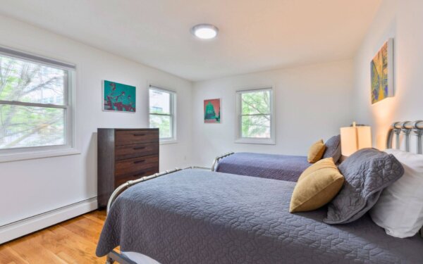 Twin bedroom with gray bedding, metal bed frames, large windows, and wall art at 235 Cardinal Medeiros, Compass Furnished Apartments.