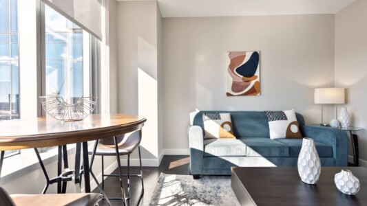 modern furnished living room in a sunny business short-term rental apartment with a tv, kitchen, spacious work desk, and high-speed internet